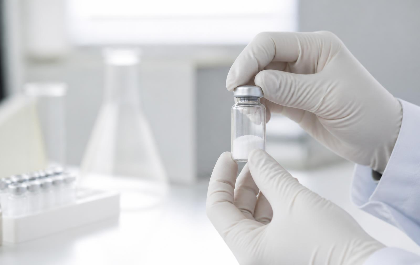A gloved researcher inspecting a sealed vial of lyophilised peptide